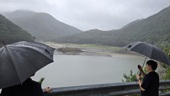 Residents holding umbrellas watch rain fall over a dry reservoir in Gangneung, Gangwon, on Sept. 13 as the city struggles with severe drought. [YONHAP]