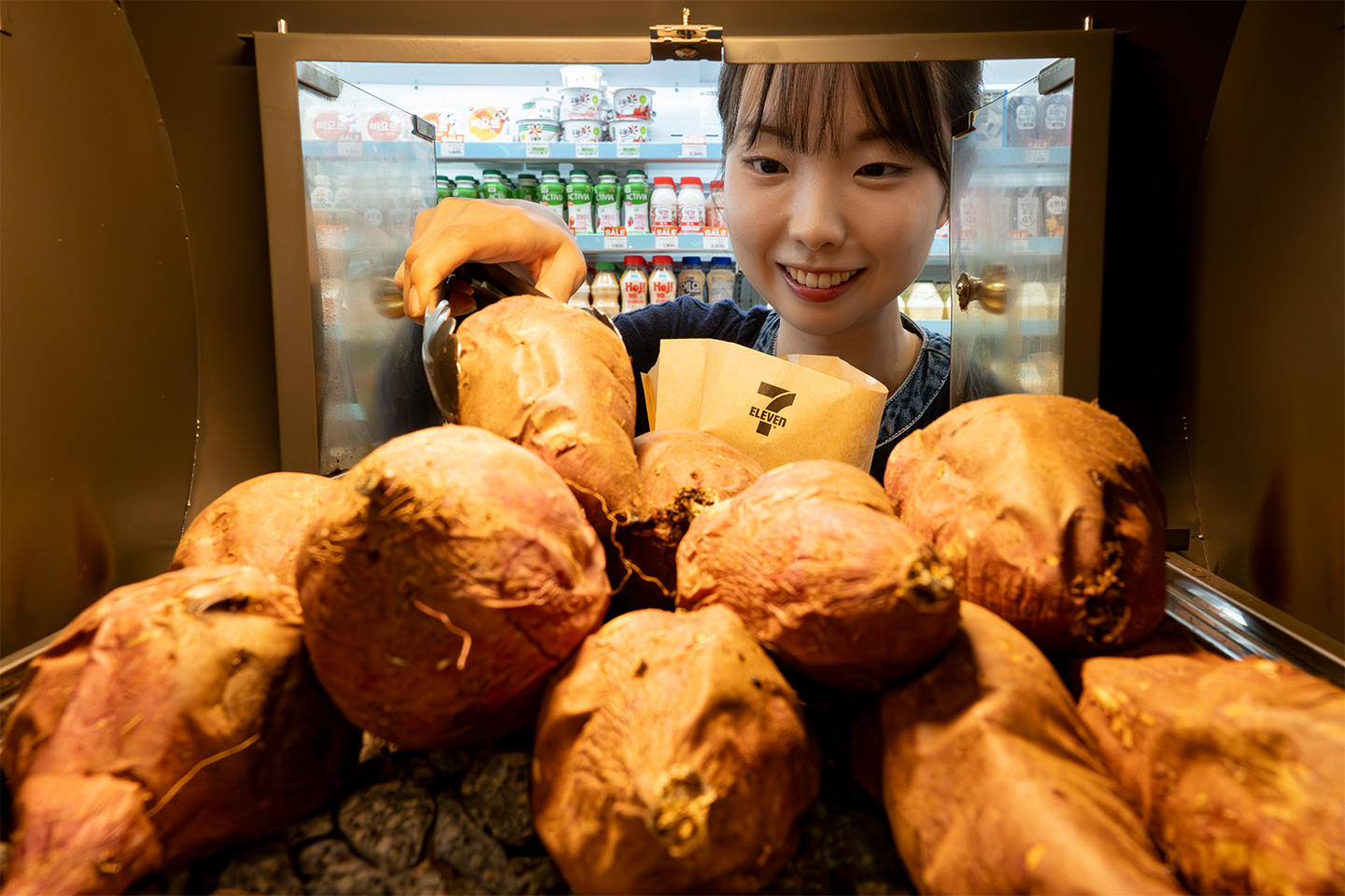 Convenience store chain 7-Eleven began selling popular winter snacks such as roasted sweet potatoes, five types of eomuk (fish cakes) and three kinds of bungeoppang (fish-shaped pastries) starting Sept. 22. A customer selects roasted sweet potatoes at a store. [7-ELEVEN]