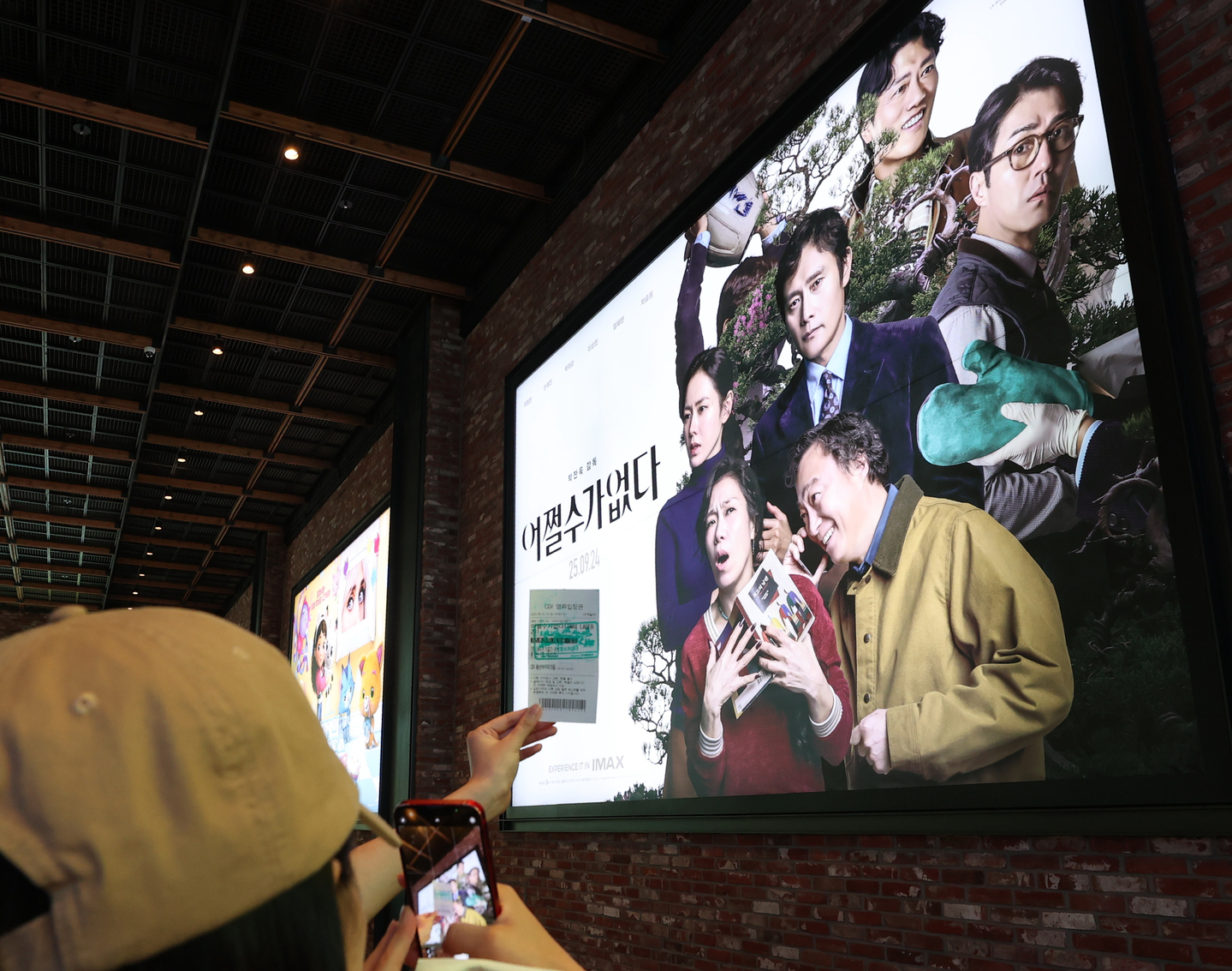 A moviegoer takes a photo of their ticket with a ″No Other Choice″ poster in the background at a Seoul cinema on Sept. 25. [YONHAP]