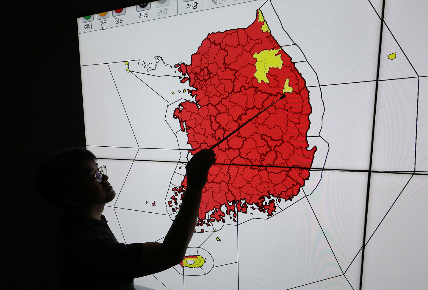 This file photo shows a weather agency official pointing to a map of Korea, with areas under a special heat wave advisory marked in red across most of the country on July 30. [YONHAP]