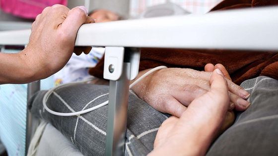 A patient’s family member holds the patient’s hand in a hospice ward at a hospital. [JOONGANG ILBO]