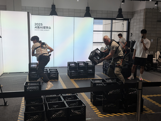 Participants move heavy racks with the aid of wearable robots during the Seoul AI Robot Show at Coex in southern Seoul on Sept. 30. [SEOUL METROPOLITAN GOVERNMENT]