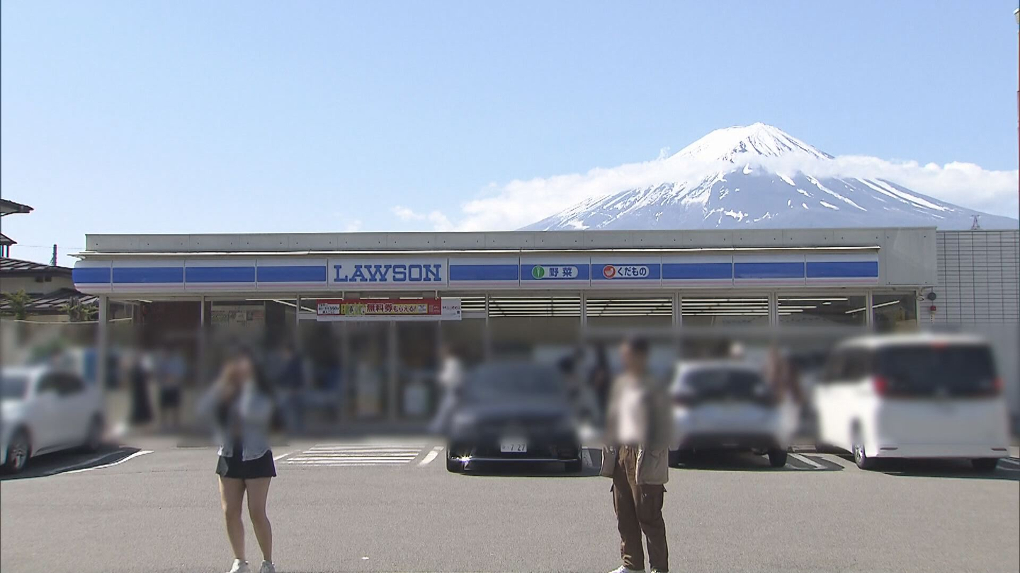 People take photos with Mount Fuji in the background at a convenience store near the mountain. [TV-ASAHI]