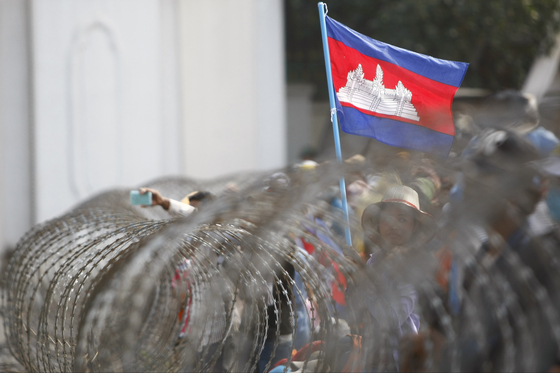 A Cambodian National flag flutters above barbed wire set up by police near the Council of Ministers building while garment workers gather for a rally in Phnom Penh, Cambodia on Dec. 30, 2013. [AP/YONHAP]