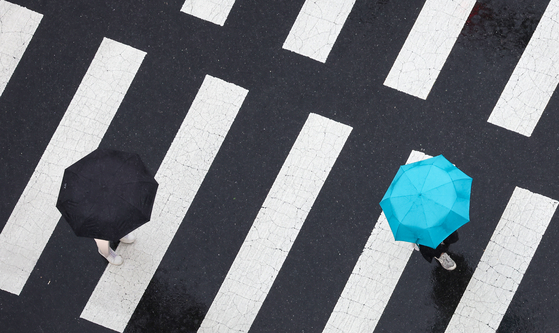 Pedestrians under umbrellas walk across a road in downtown Seoul on Sept. 16. [YONHAP] 