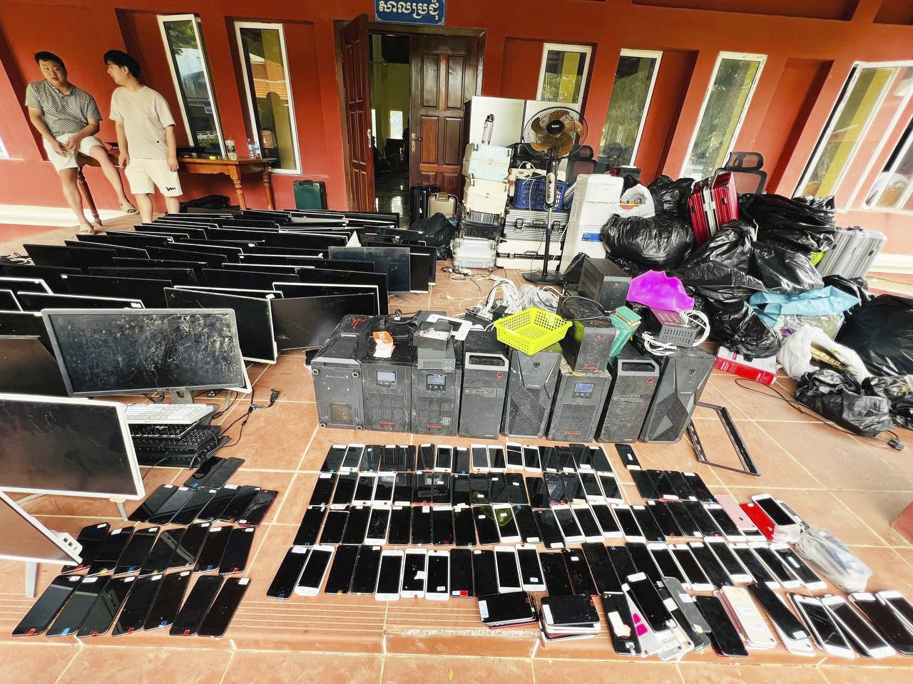 In this photo provided by state news service Agence Kampuchea Press, alleged online scammers stand next to their tools collected by authorities at its site in a classroom on the outskirts of Phnom Penh, Cambodia, Friday, July 18, 2025. [AP/YONHAP]