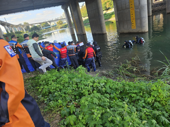 A search team from the National 119 Rescue Headquarters retrieves a body found around 9 a.m. on Oct. 17 near Dongmak Bridge over the Jungnang Stream in Uijeongbu, Gyeonggi, and hands it over to police. [GYEONGGI NAMBU FIRE AND DISASTER HEADQUARTERS]