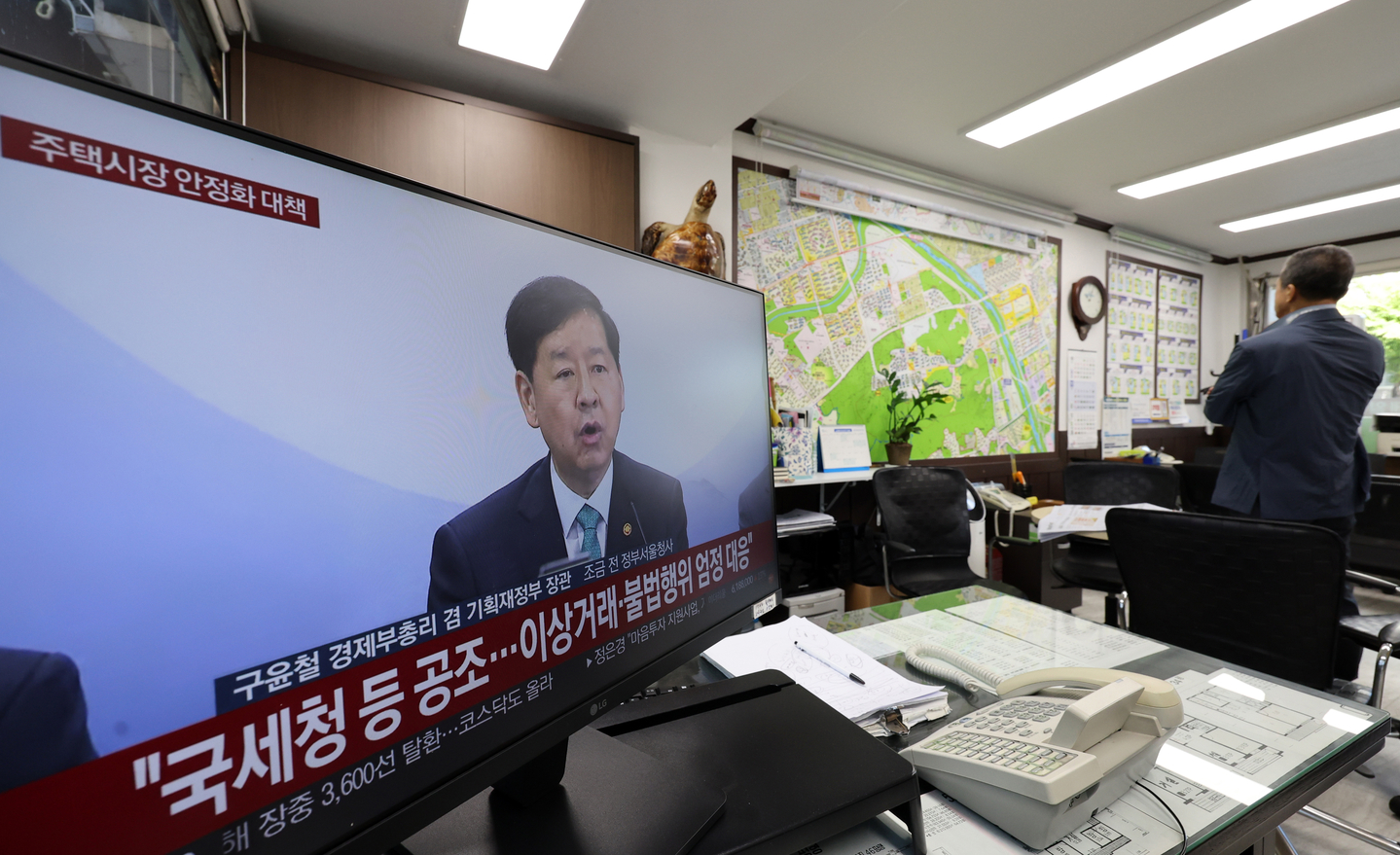 A television at a real estate agency in Seoul airs news coverage of the government’s new housing market stabilization measures on Oct. 15. All 25 districts of Seoul and 12 cities in Gyeonggi Province have been newly designated as regulated zones, including areas subject to heightened transaction and speculation controls. [YONHAP]