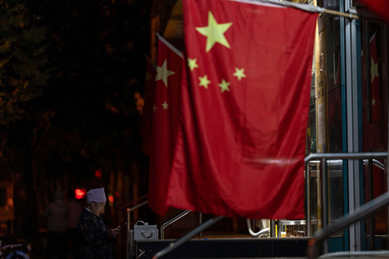 An elderly woman stands near Chinese national flags hung for the national day holidays during the mid-autumn festival in Beijing on Oct. 6. [AP/YONHAP]