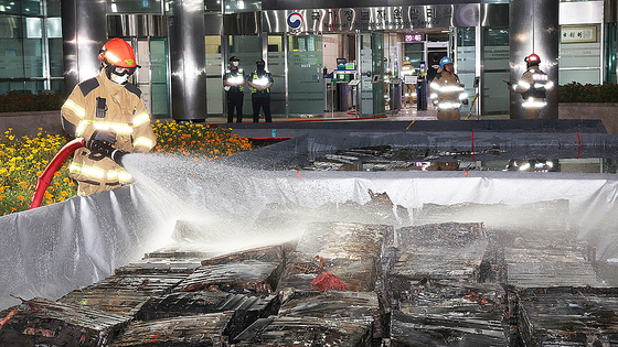 A firefighter sprays water on fire-damaged lithium-ion batteries in a water tank at the National Information Resources Service in Yuseong District, Daejeon, on the night of Sept. 27. [YONHAP]