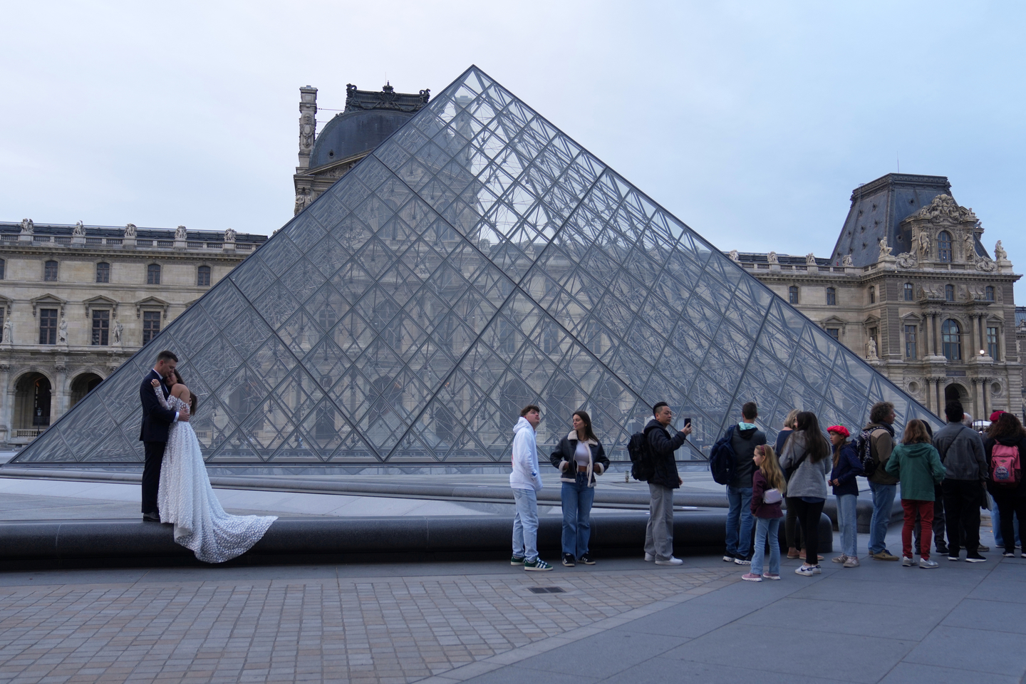 A wedding couple hugs as visitors queue to enter the Louvre museum three days after historic jewels were stolen in a daring daylight heist, on Oct. 22 in Paris. [AP/YONHAP]