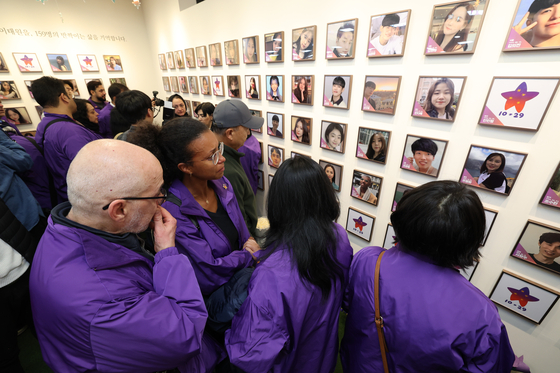 Family members of victims of the 2022 Itaewon crowd crush shed tears as they hang photos of their loved ones on a wall during a visit to the House of Stars in Jongno District, central Seoul, on Oct. 26. [JOINT PRESS CORPS]