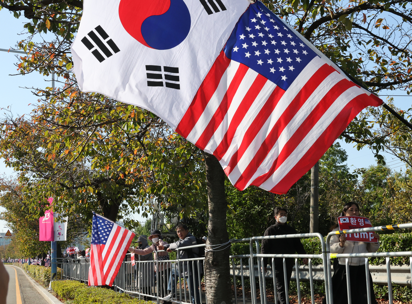 Crowds wave U.S. and Korean flags to welcome U.S. President Donald Trump on the access road to Gimhae International Airport in Busan’s Gangseo District on Oct. 29, as police maintain tight security. [SONG BONG-GEUN] 
