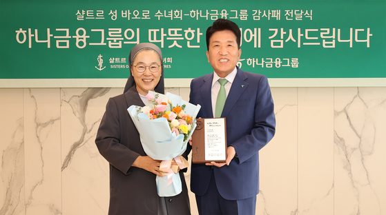 Hana Financial Group Chairman Ham Young-joo, right, receives a plaque of appreciation from Sisters of St. Paul of Chartres Provincial Superior Min Hye-sook on Friday at the Hana Financial Group headquarters in Myeong-dong in central Seoul. [HANA FINANCIAL GROUP]