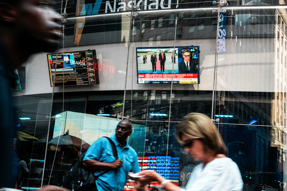 People walk near a screen showing U.S. President Donald Trump meeting with Russian President Vladimir Putin in Alaska, at the Nasdaq Market site in New York City, U.S., Aug. 15, 2025. [REUTERS/YONHAP]