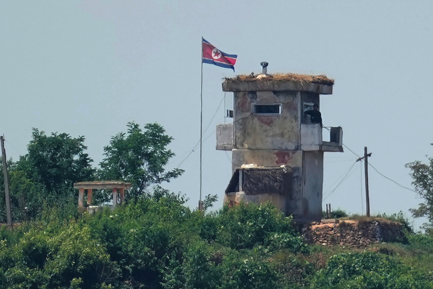 A soldier stands at a North Korean military guard post flying a national flag, seen from Paju, Gyeonggi on June 26, 2024. [AP/YONHAP] 