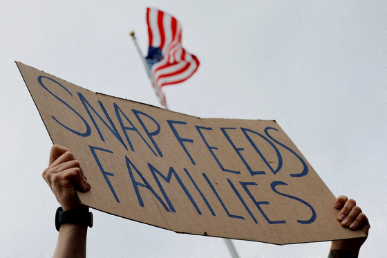 A man holds a sign reading ″SNAP Feeds Families,″ as food aid benefits come under threat due to the ongoing U.S. government shutdown, during ″A Rally for SNAP″ on the steps of the Massachusetts Statehouse in Boston, Massachusetts, on Oct. 28. [REUTERS/YONHAP]