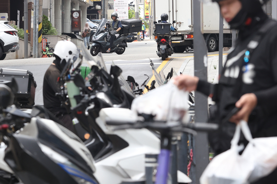 Delivery workers pick up food parcels from restaurants at a street in Gangnam District, southern Seoul on June 17. [YONHAP]