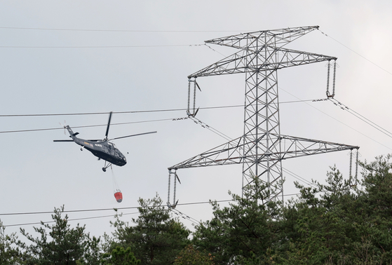 A helicopter passes by a transmission tower in Ulsan on March 27. [YONHAP]