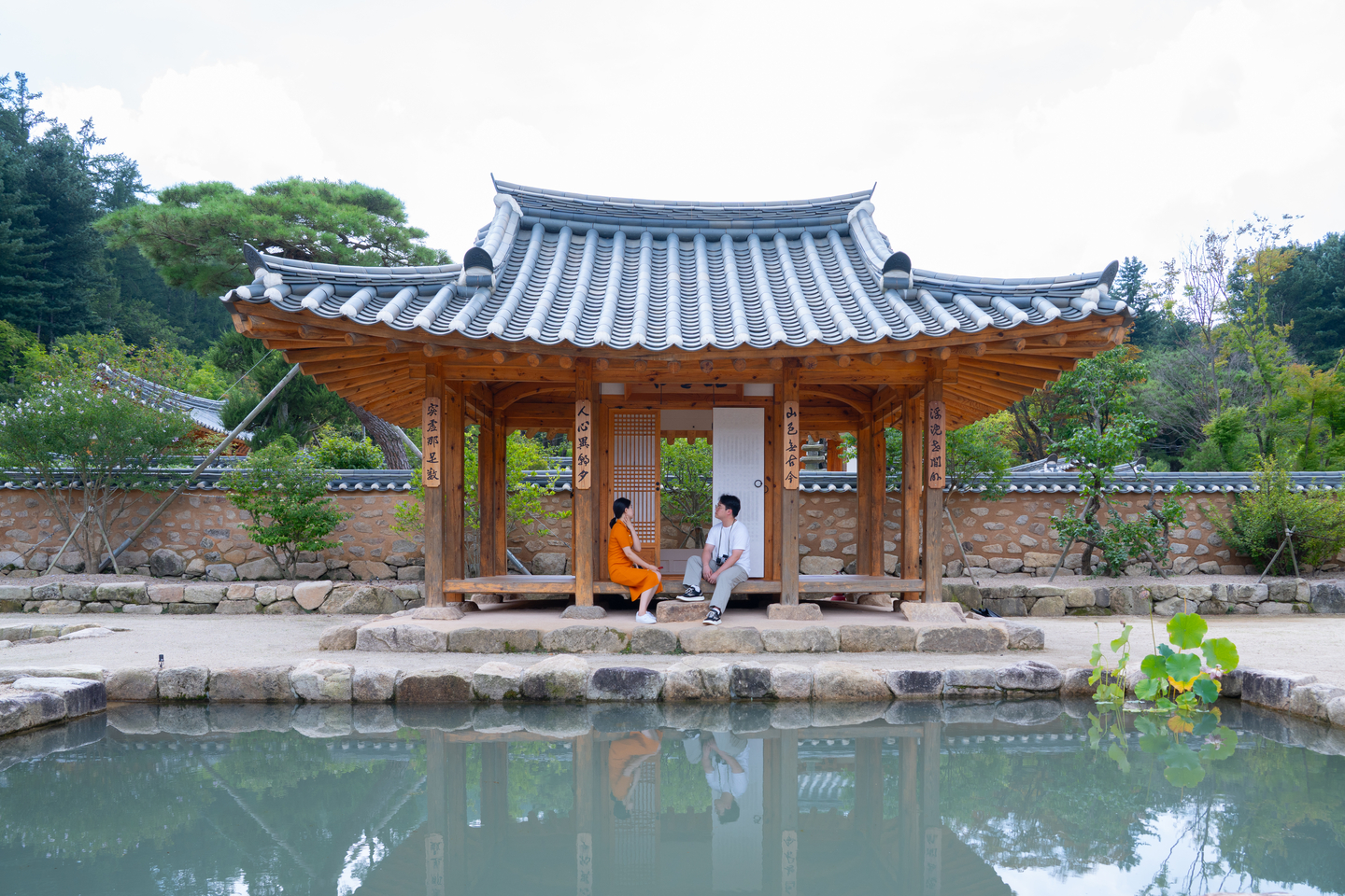 Two people sit on a pavilion behind the square-shaped Hamso Pond.[JOONGANGILBO]