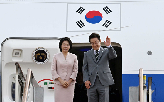 President Lee Jae Myung, right, and first lady Kim Hea Kyung wave to reporters before boarding the presidential airplane at the Seoul Air Base in Seongnam, Gyeonggi, for their trip to the Asean 3 on Oct. 26. [JOINT PRESS CORPS]