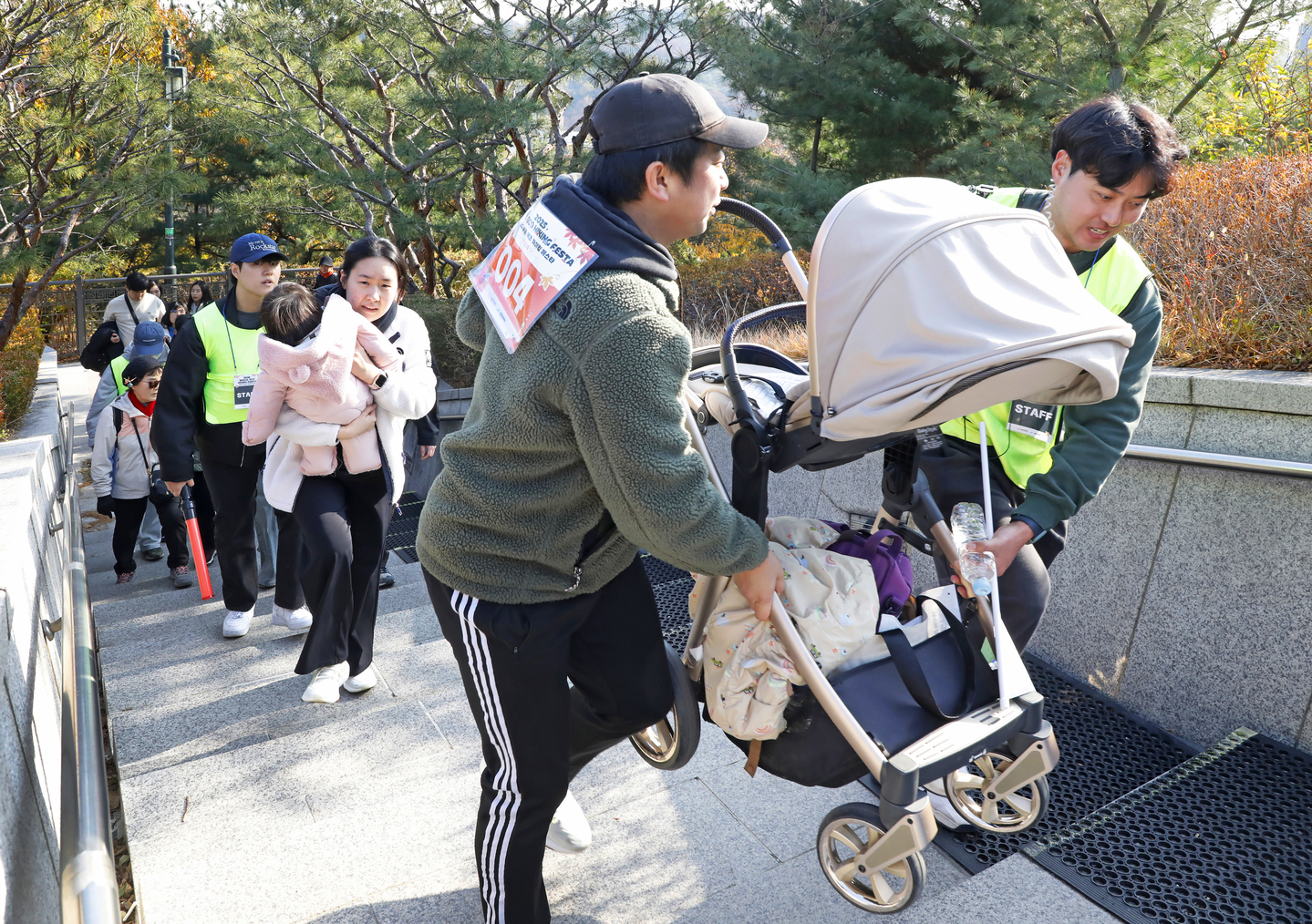 A staffer helps a participant of the 2025 Seoul Eco Hiking Festa move a stroller along a trail on Mount Namsan in Jung District, central Seoul, during the event’s family-themed hike on Nov. 22. [PARK SANG-MOON]