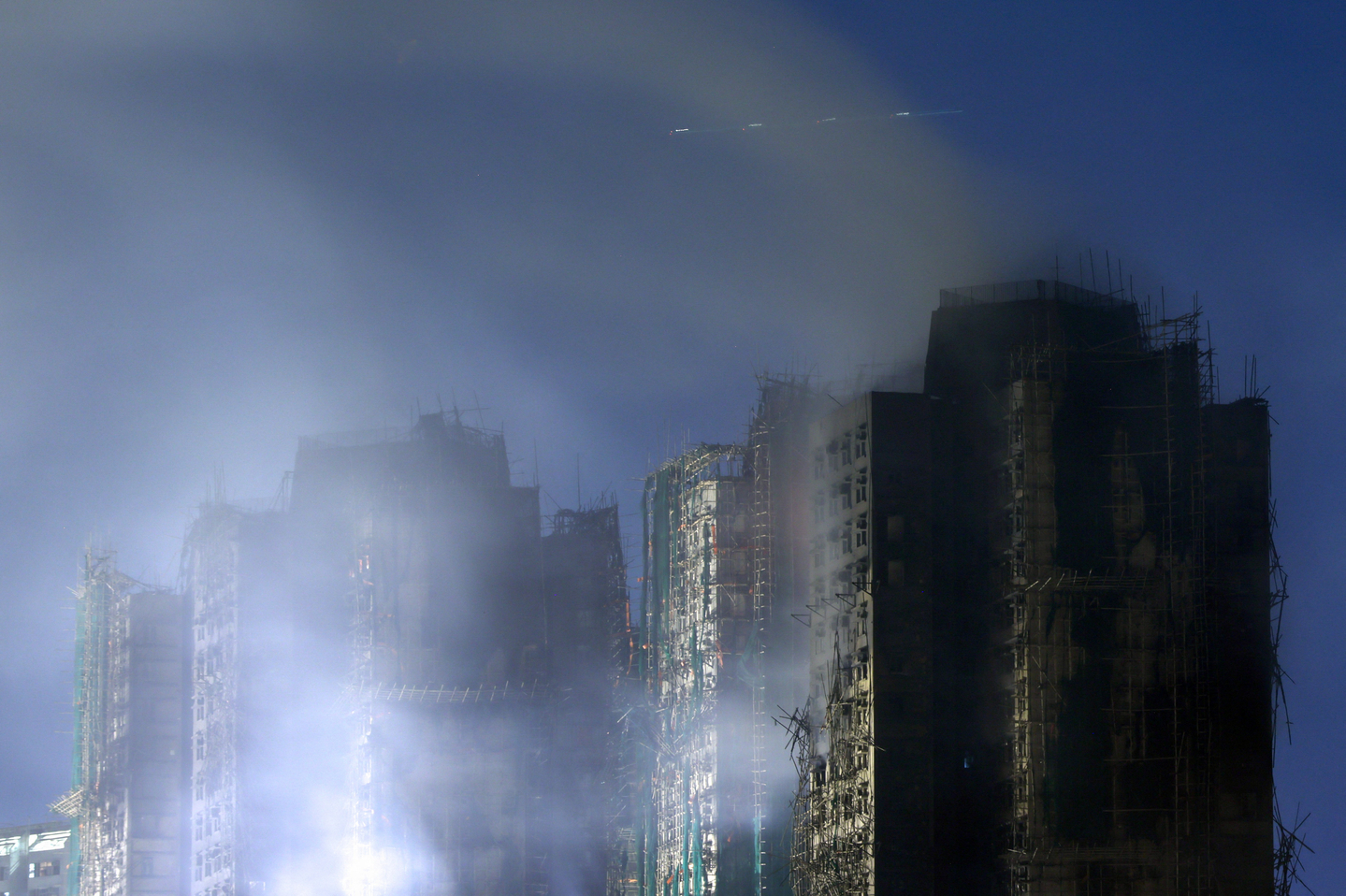 A plane flies overhead as smoke rises from a deadly fire, which broke out on Nov. 26 at Wang Fuk Court housing complex in Hong Kong on Nov. 27. [REUTERS/YONHAP]