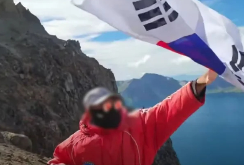 A Korean YouTuber waves a Taegeukgi at Heaven Lake on Mount Paektu. [SCREEN CAPTURE]
