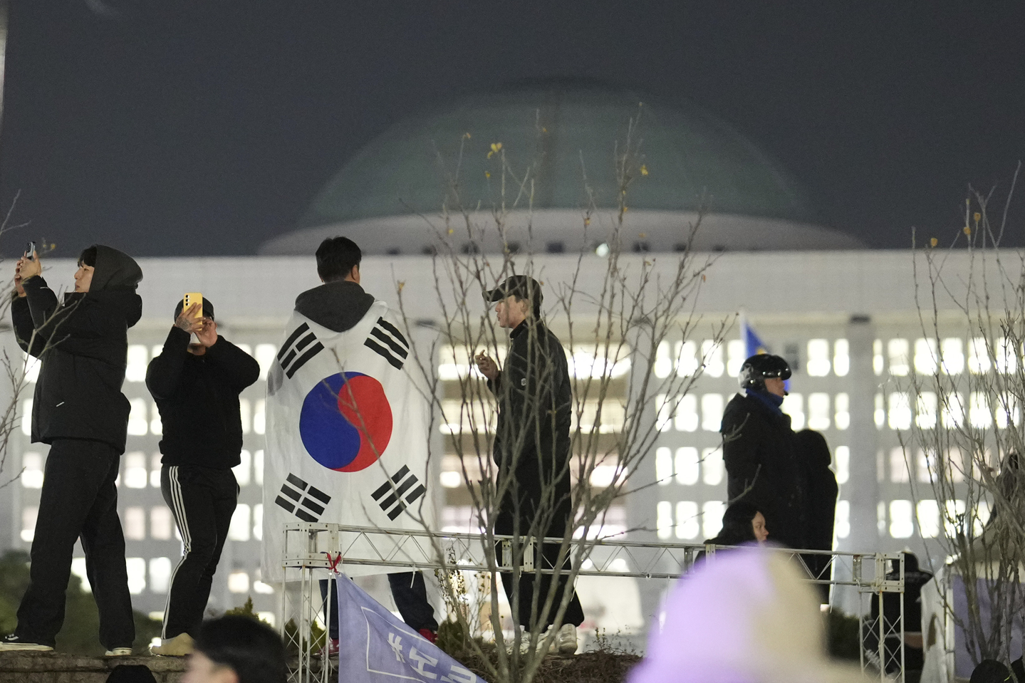 A man with the Korean flag draped over his shoulders stands on the wall of the National Assembly in Yeouido, western Seoul, in the early hours of Dec. 4, 2024. [AP/YONHAP]