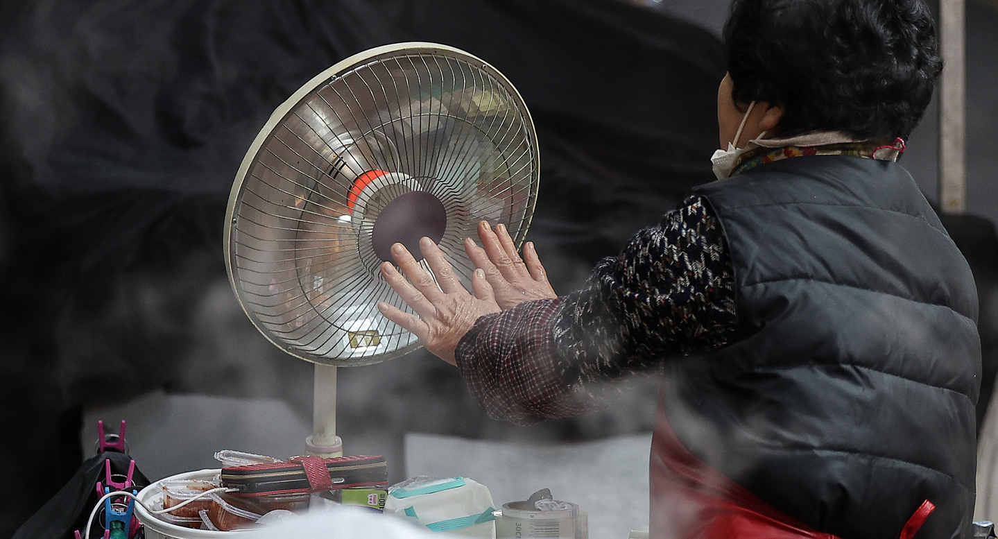 A market stall owner warms her hands in front of a heater at a traditional market in Daegu on Dec. 3. [YONHAP]