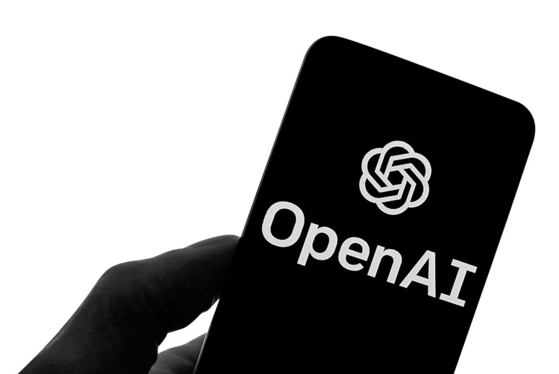 The OpenAI logo is seen on a mobile phone in front of a computer screen displaying output from ChatGPT on March 21, 2023. [AP/YONHAP] 