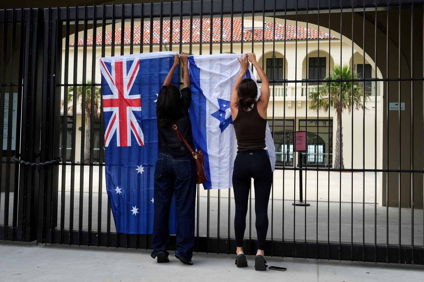 Women place an Israeli flag next to an Australian flag on a gate outside Bondi Pavilion at Sydney's Bondi Beach, Dec. 15, a day after a shooting. [AP/YONHAP]