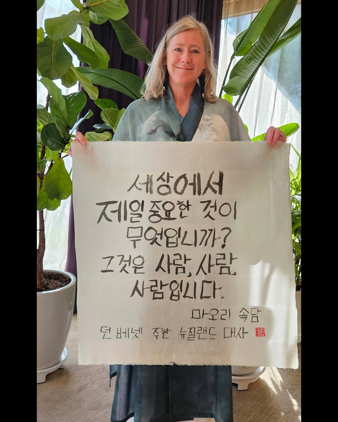 New Zealand Ambassador to Korea Dawn Bennet poses with a Korean calligraphy piece featuring a Maori proverb that reads, “What is the most important thing in the world? It is the people, it is the people, it is the people,” at the New Zealand residence in a photo posted on the social media of the New Zealand Embassy in Seoul on July 11. Bennett has said the message resonates strongly in Korea, reflecting shared values around community and respect for people. [SCREEN CAPTURE]