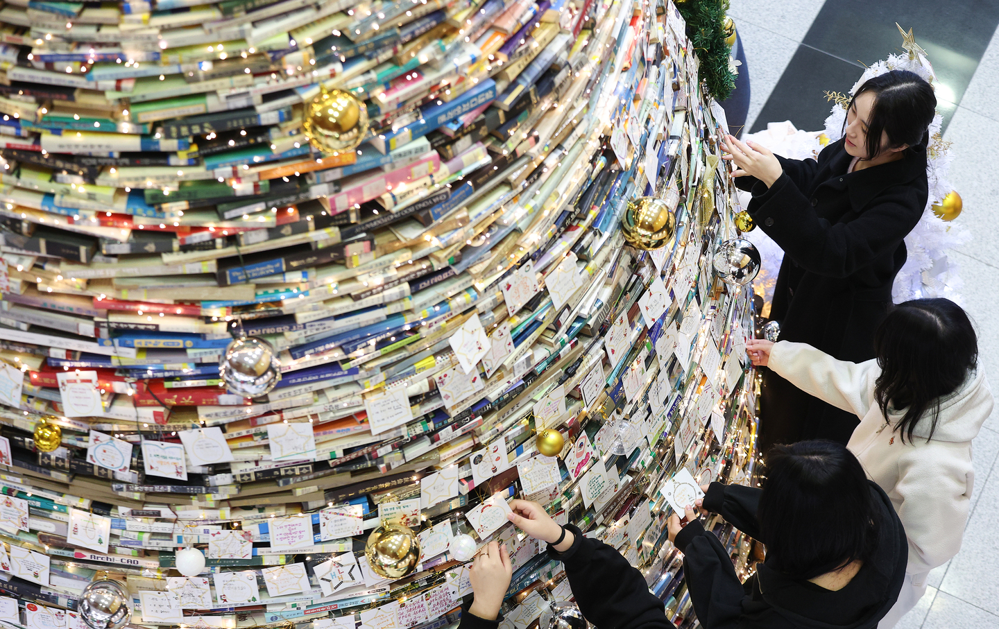 Students attach handwritten wishes to a Christmas tree made out of books at Changpa Library on Daegu University’s Gyeongsan campus on Dec. 16. [YONHAP]