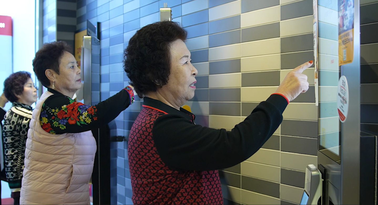 Elderly participants practice placing orders using a self-service kiosk during a training session at a fast-food restaurant in the greater Seoul area. [NATIONAL INSTITUTE FOR LIFELONG EDUCATION] 