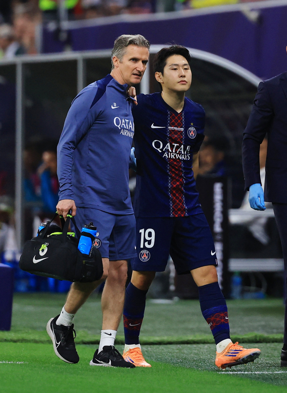 Lee Kang-in of Paris Saint-Germain, right, leaves the field with the help of a team trainer after being substituted due to a left hamstring injury during the final of the FIFA Intercontinental Cup against CR Flamengo at Ahmad bin Ali Stadium in Al Rayyan, Qatar, on Dec. 17. [REUTERS/YONHAP]