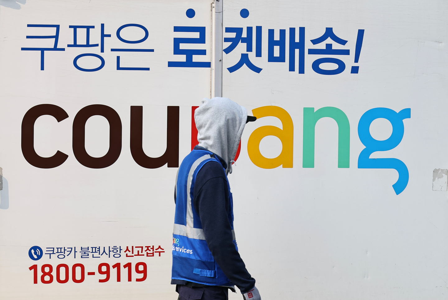 A Coupang worker walks in front of a delivery truck with the company logo printed on it in a logistics center in Seoul on Dec. 17. [YONHAP]