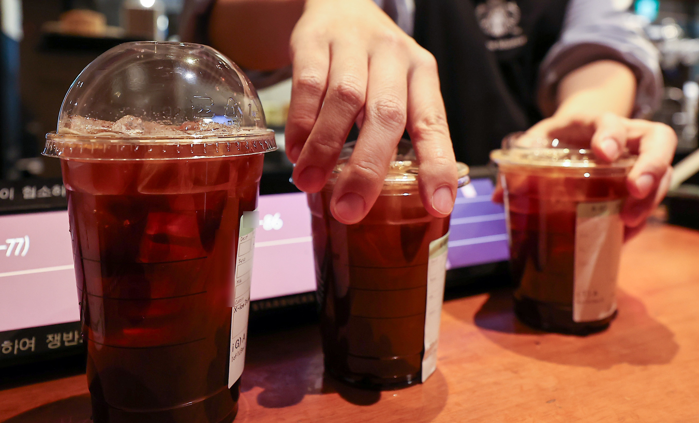 A worker organizes disposable plastic cups filled with coffee at a cafe in Seoul on Dec. 18. [NEWS1]
