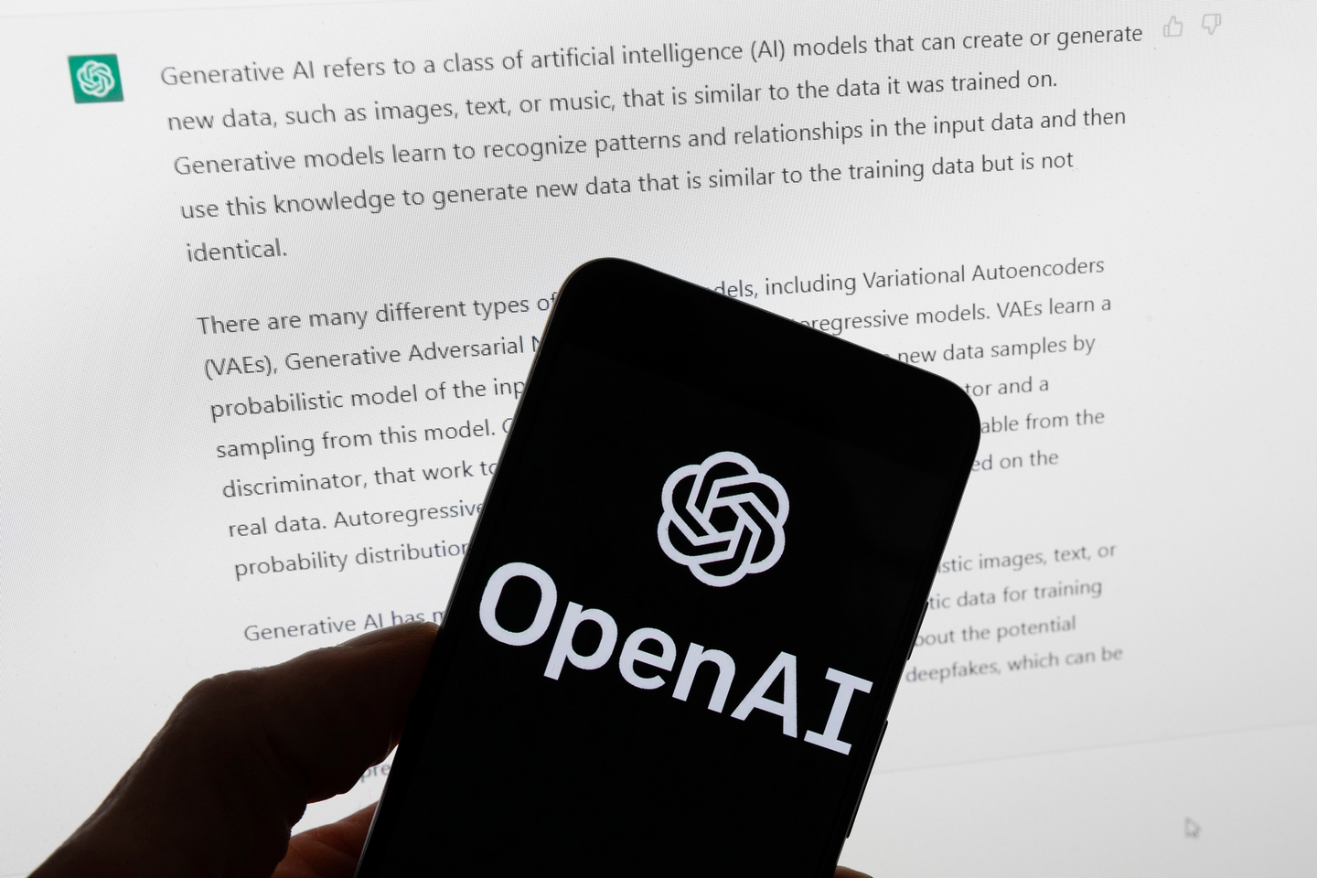 The OpenAI logo is displayed on a mobile phone in front of a computer screen with output from ChatGPT in Boston on March 21, 2023. [AP/YONHAP]