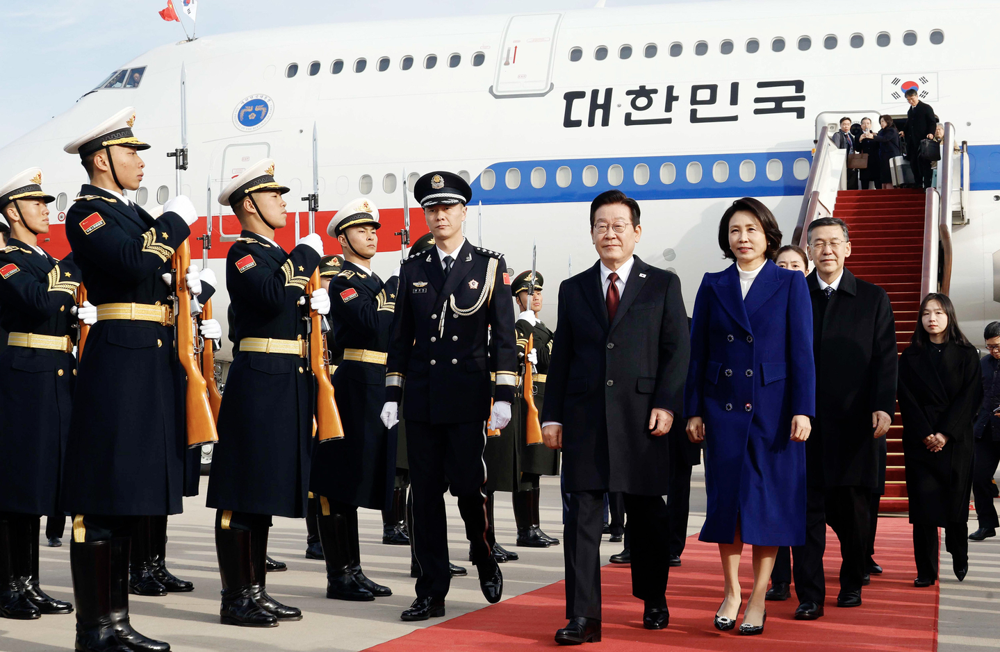 President Lee Jae Myung, center left, and first lady Kim Hea Kyung, center right, walk down a red carpet upon arriving at Beijing Capital International Airport in Beijing on Jan. 4, kicking off a four-day state visit to China. [JOINT PRESS CORPS]
