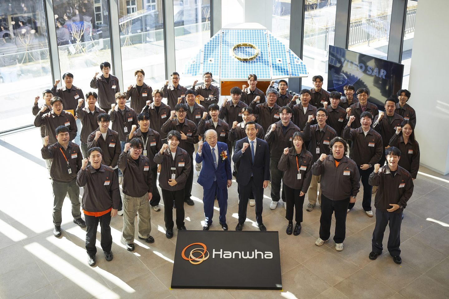 Hanwha Group Chairman Kim Seung-youn and Vice Chairman Kim Dong-kwan, both center in front row, pose for a photo with employees of Hanwha Systems at the Hanwha Space Center on Jeju Island on Jan. 8, in front of a full-scale model of the ultra-high-resolution synthetic-aperture radar satellite in very low Earth orbit. [HANWHA GROUP]