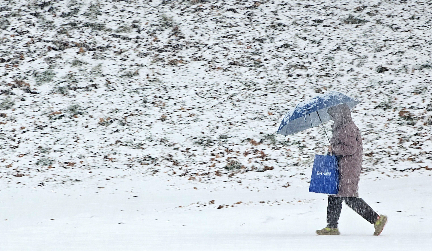 A person walks underneath an umbrella as snow falls in Chuncheon, Gangwon on Dec. 23, 2025. [YONHAP]
