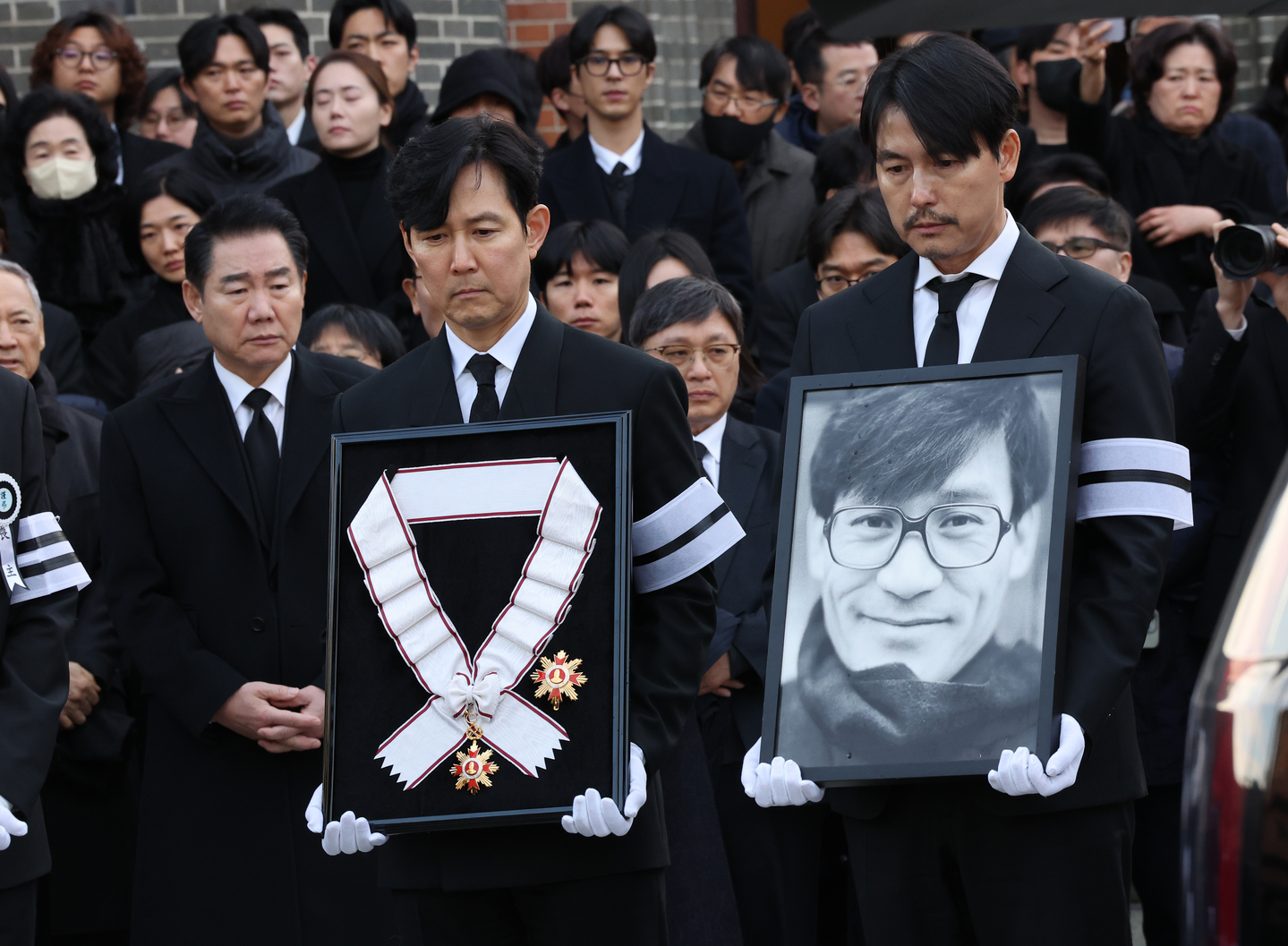 Actors Jung Woo-sung, carrying Ahn's portrait at right, and Lee Jung-jae, holding the Geumgwan Order of Cultural Merit, the country's highest cultural honor that was posthumously awarded to the actor, lead the funeral procession of late actor Ahn Sung-ki at the Myeongdong Cathedral in central Seoul on Jan. 9. [YONHAP]