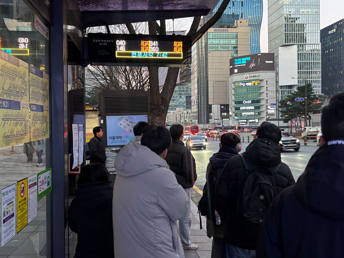 Passengers wait for a bus at a bus stop in Gangnam District, southern Seoul, at 7 a.m. on Jan. 13. With city bus service halted due to the strike, the electronic display shows the bus location as “depot.” [RYU HYO-RIM]