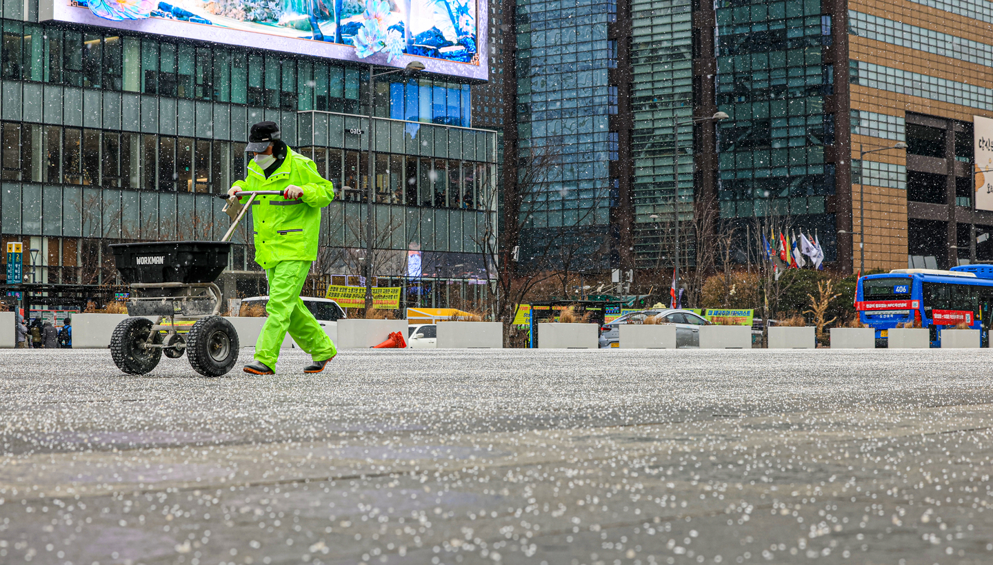 Workers spread calcium chloride at Gwanghwamun Square in central Seoul on Jan. 12 as snow falls. [NEWS1]