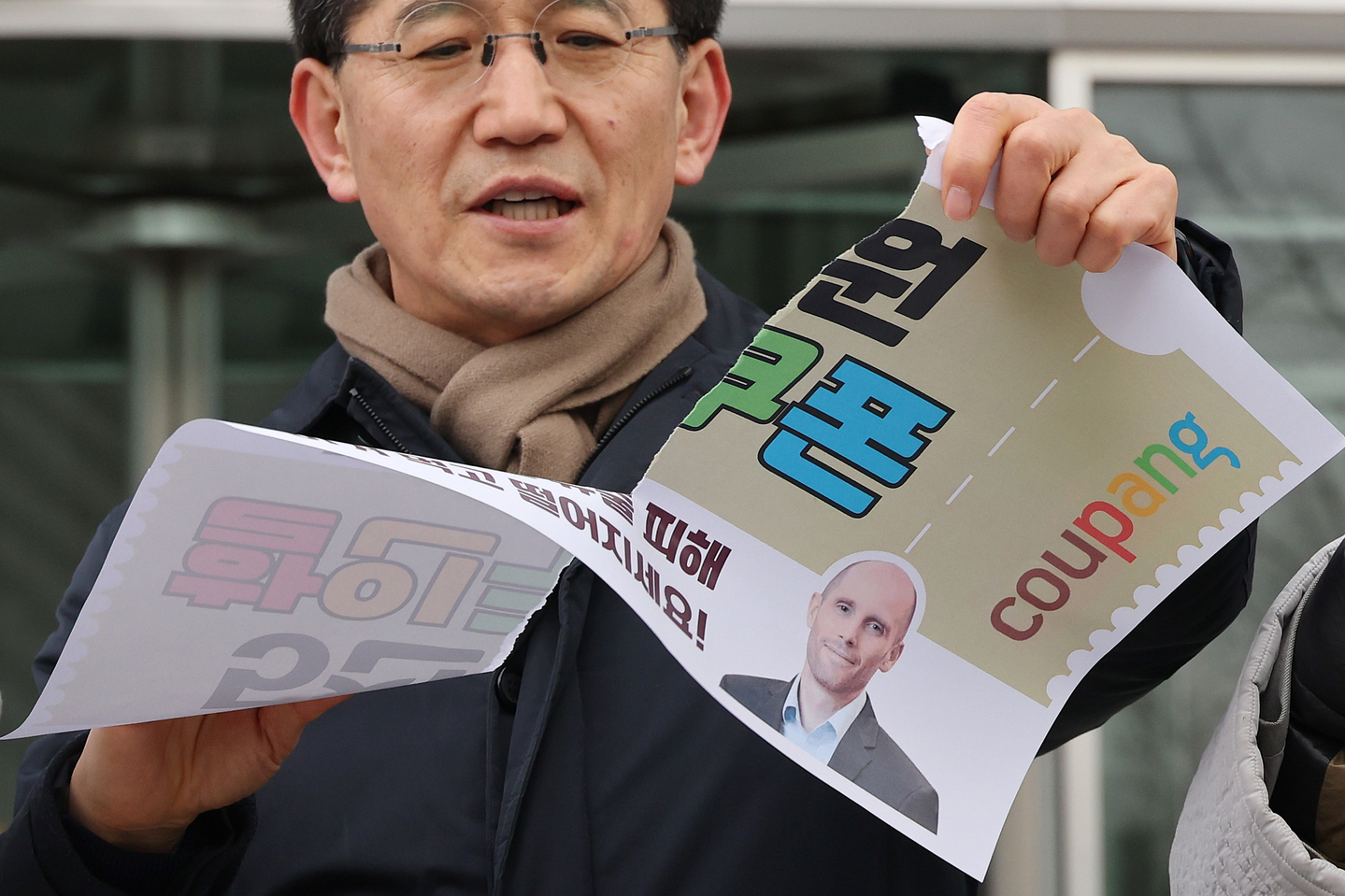 A member of a civic group protesting Coupang's security practices tear up posters that resemble 5,000-won ($3) coupons during a news conference titled “Declaration rejecting Coupang vouchers and Coupang withdrawals that deceive the public” in front of Coupang’s headquarters in Songpa District, southern Seoul, on Jan. 14. [YONHAP]