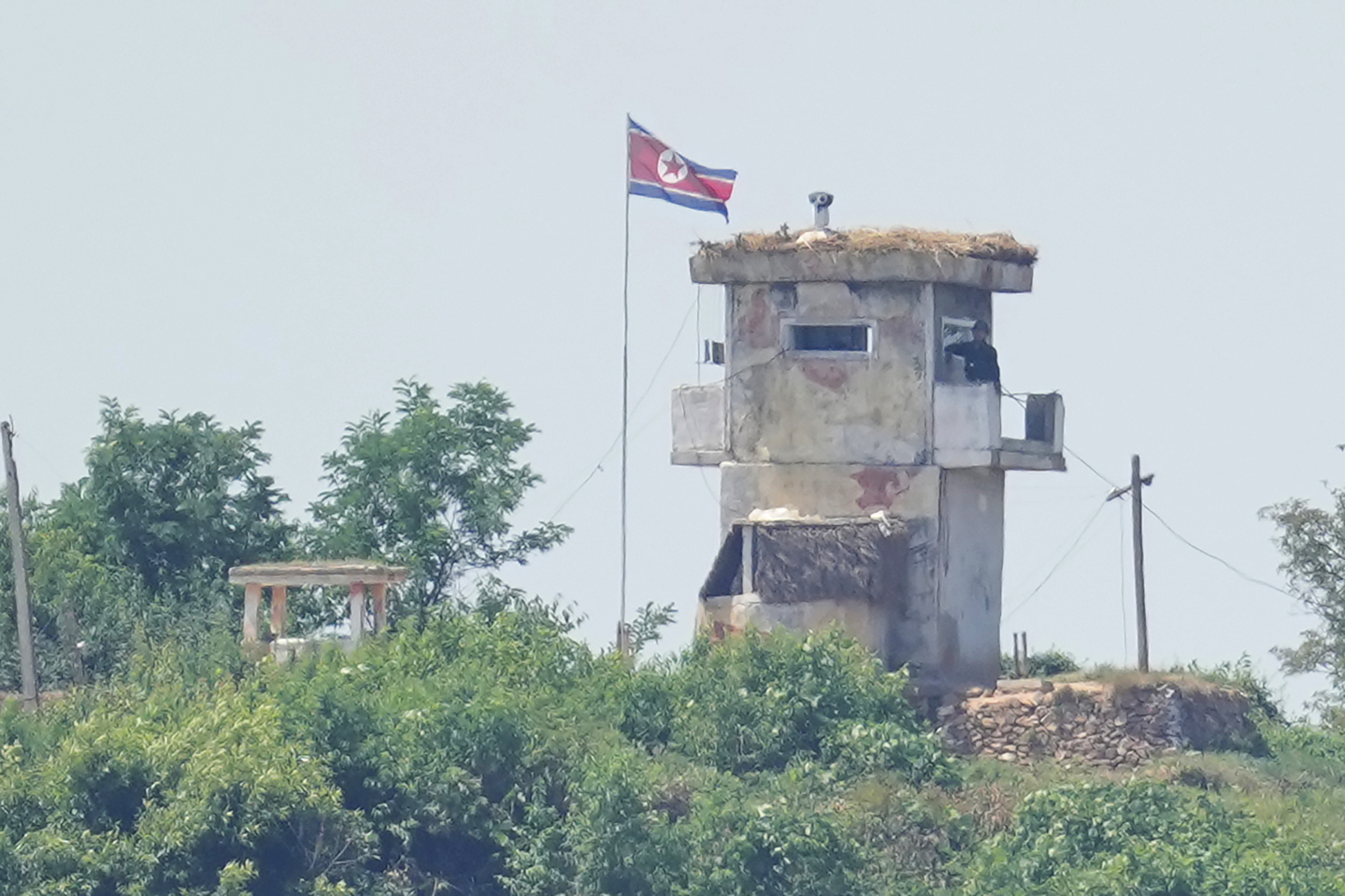 A soldier stands at a North Korean military guard post flying a national flag, seen from Paju, Gyeonggi on June 26, 2024. [AP/YONHAP] 