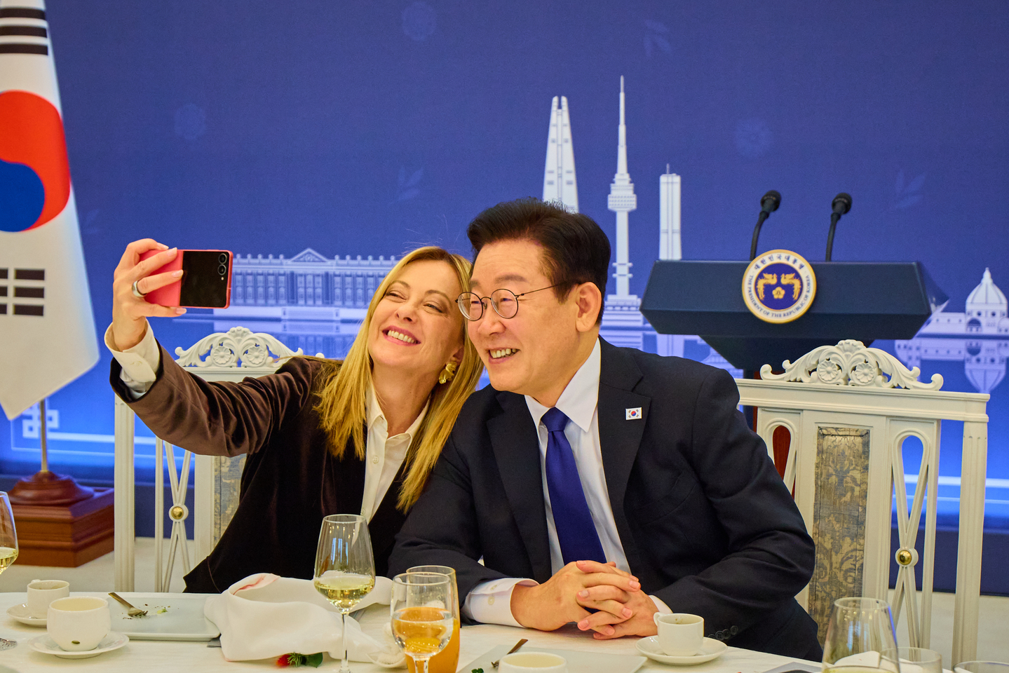 Italian Prime Minister Giorgia Meloni, left, takes a selfie with President Lee Jae Myung with a Samsung Galaxy Z Flip7 gifted by the Korean leader at an official luncheon following their bilateral summit at the Blue House in central Seoul on Jan. 19. [JOINT PRESS CORPS]