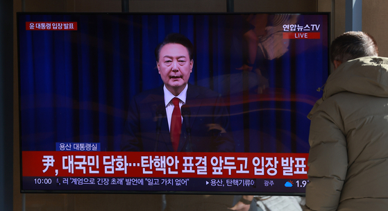 A member of the public watches President Yoon Suk Yeol's address to the nation on a screen in Seoul Station in central Seoul on Dec. 7.  [YONHAP]