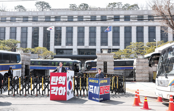 An official from the conservative People Power Party, left, holds a sign calling for President Yoon Suk Yeol's reinstatement, while a member of the liberal Democratic Party, right, holds a sign calling for his removal from office in front of the Constitutional Court in Jongno District, central Seoul, on March 23. [JOONGANG ILBO]